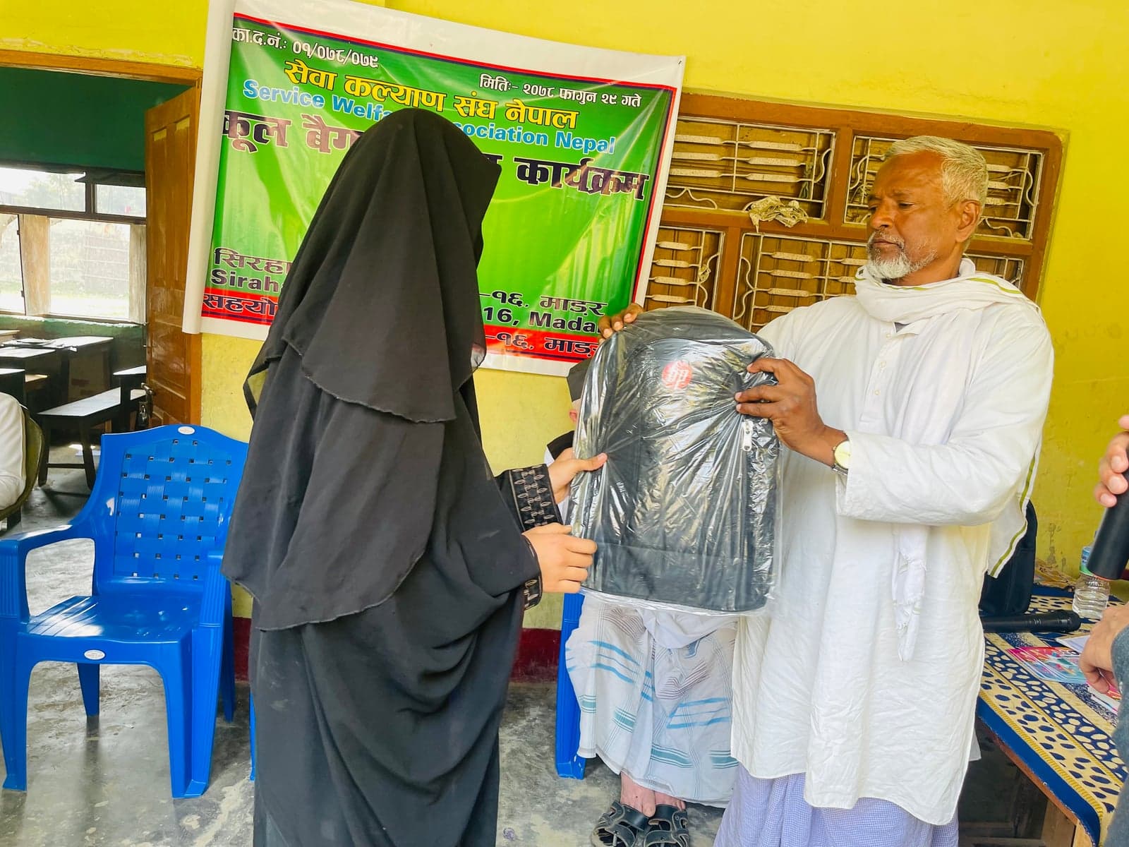A participant and an adult hold a wrapped school bag beside a SWAN banner.